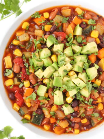 Vegan summer vegetable chili in a white bowl with avocado