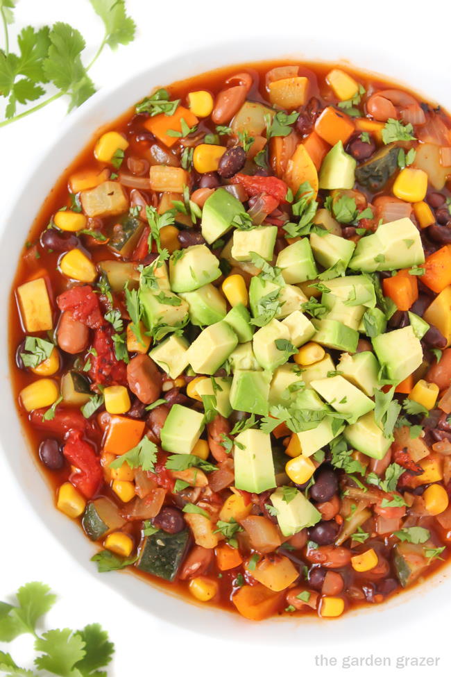 Vegan summer vegetable chili in a white bowl with avocado