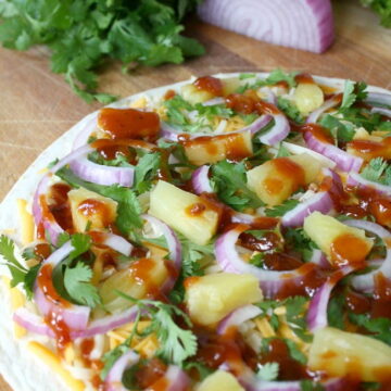 Open-faced BBQ quesadilla on a cutting board with cilantro and onion
