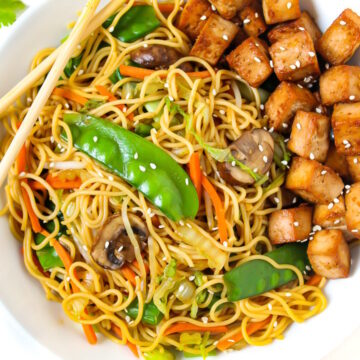 Vegan vegetable lo mein on a white serving plate with baked tofu and chopsticks