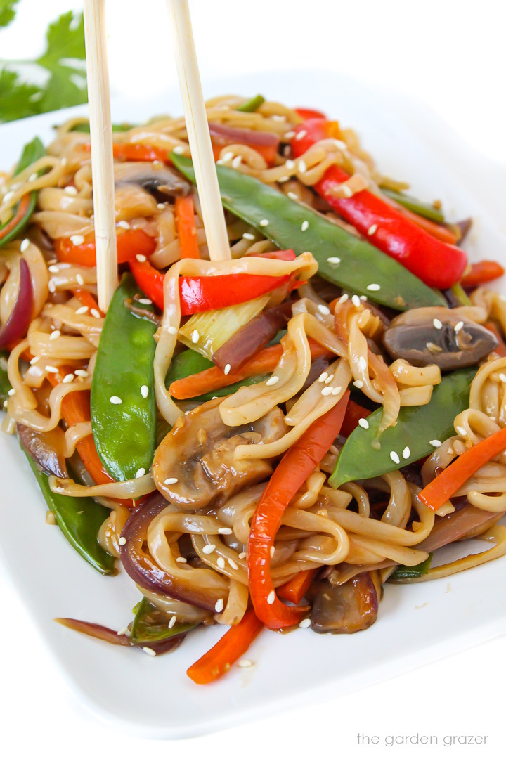 Close-up view of vegetable lo mein on a white plate with chopsticks
