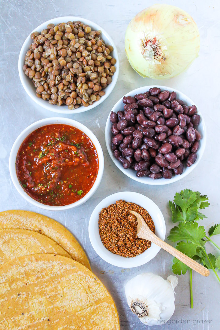 Corn tortillas, beans, onion, salsa, garlic, fresh cilantro, and taco seasoning ingredients laid out on a metal tray