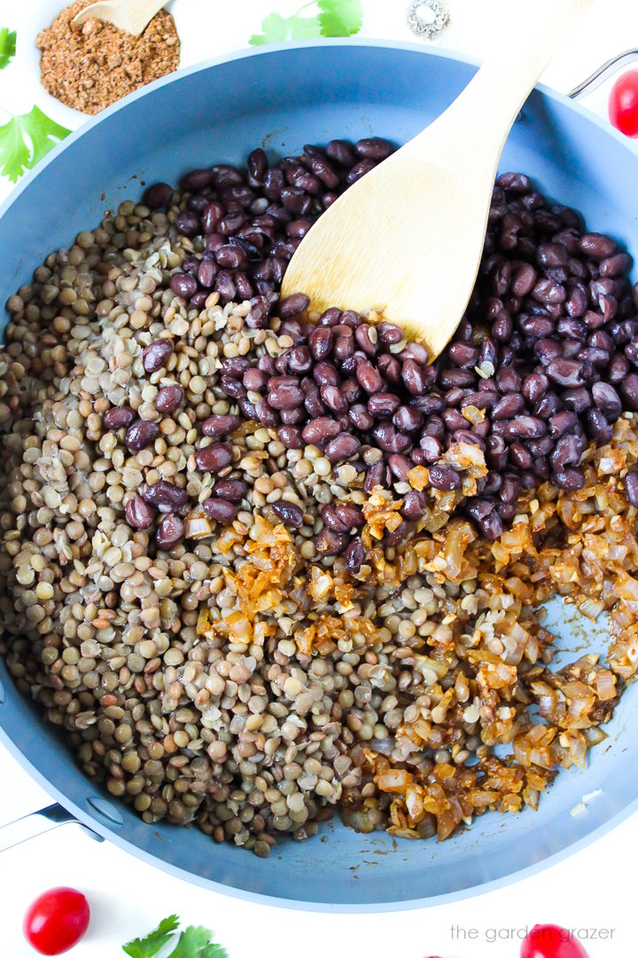 Overhead view of preparing vegan taco mixture in a large skillet with wooden spoon