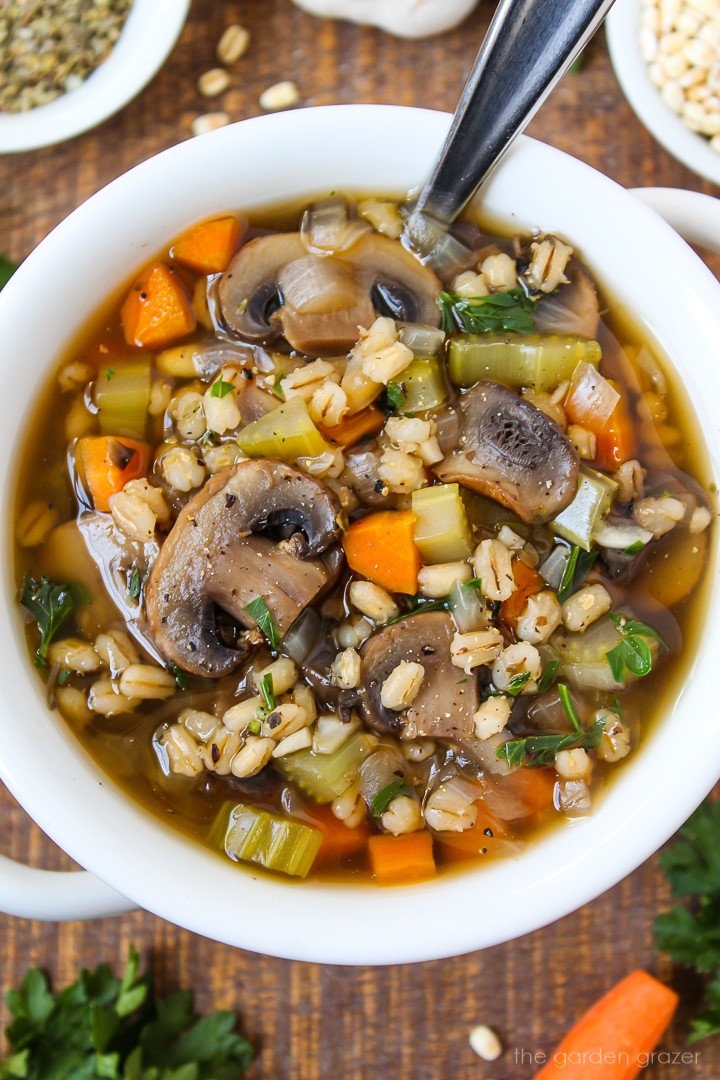 Close up view of mushroom barley soup in a white serving bowl with spoon