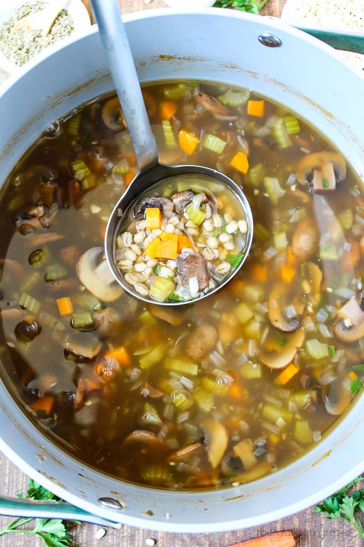 A ladle lifting up mushroom barley soup as it cooks in a large stockpot