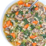 Vegan mushroom barley soup with kale in a bowl with spoon