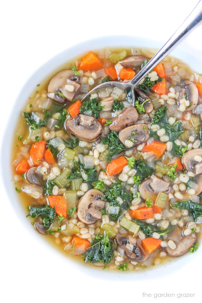 Vegan mushroom barley soup with kale in a bowl with spoon