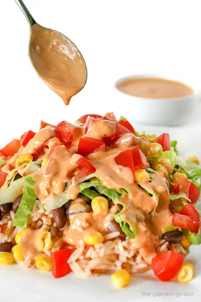 Vegan burrito bowl on a plate being drizzled with chipotle dressing