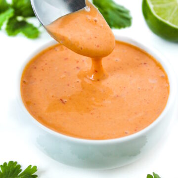Spoon lifting up creamy yogurt chipotle sauce from a small white bowl