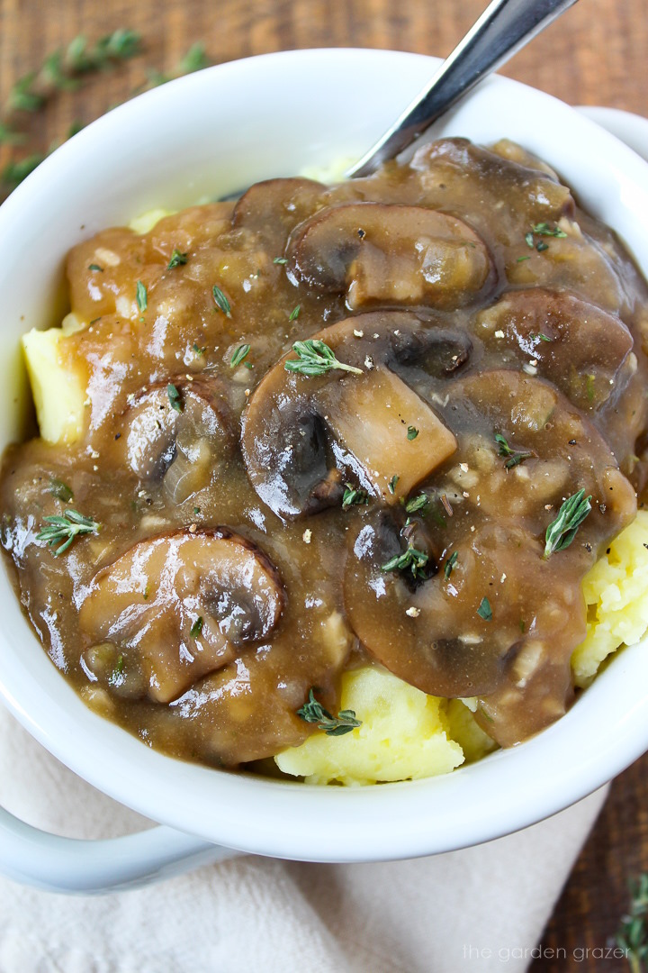 Close up view of vegan mushroom gravy spooned over mashed potatoes in a white serving bowl