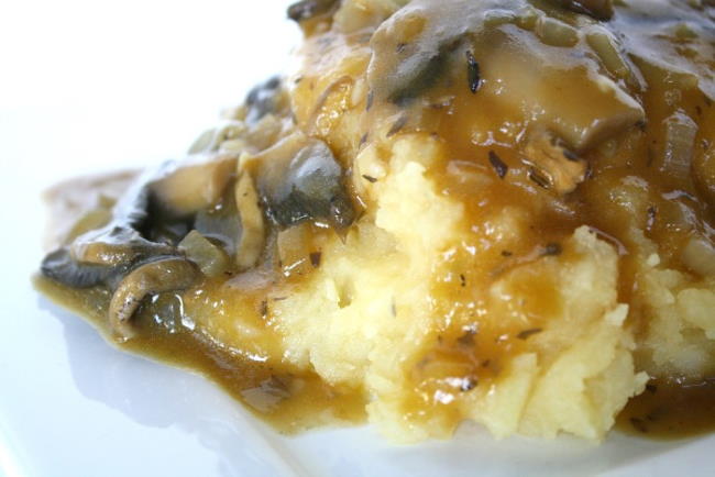 Vegan mushroom gravy poured over mashed potatoes on a white plate