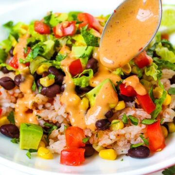 A spoon drizzling creamy chipotle sauce over a vegan black bean burrito bowl on a white plate