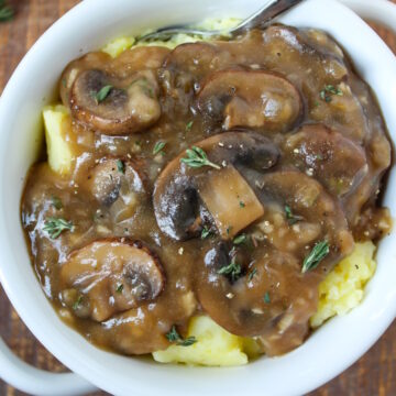 Vegan mushroom gravy over mashed potatoes in a white serving bowl with spoon