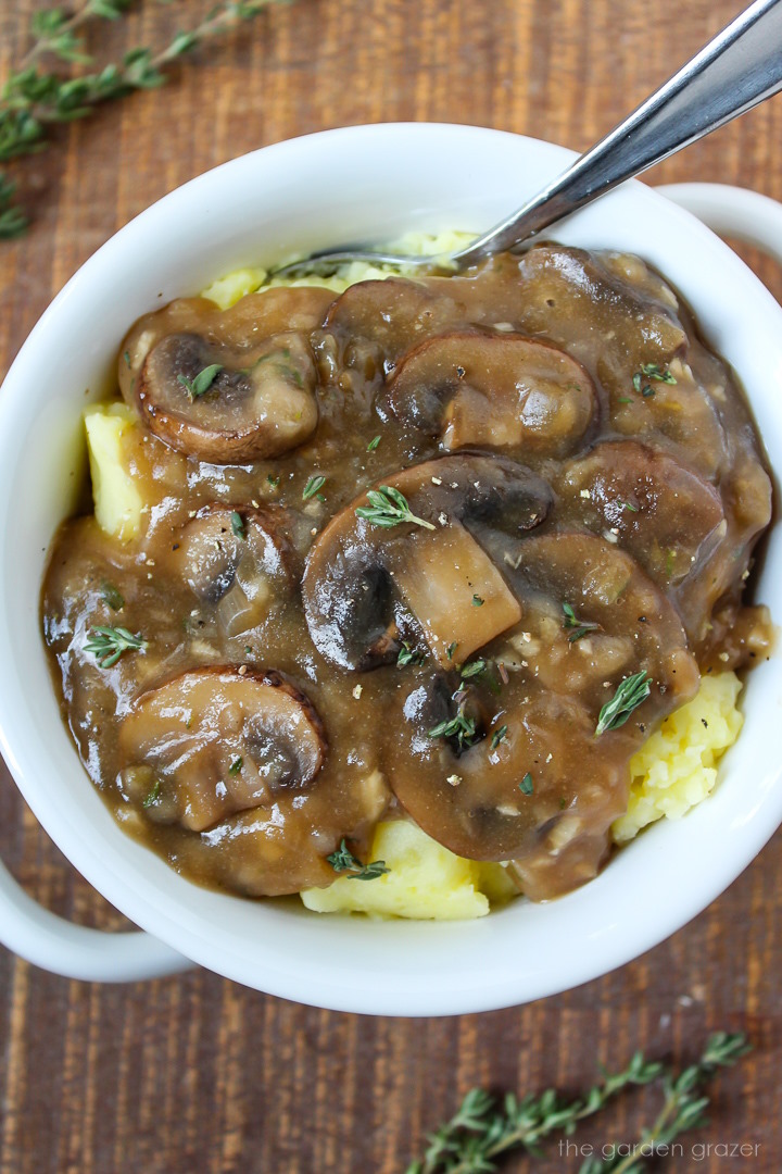 Vegan mushroom gravy over mashed potatoes in a white serving bowl with spoon