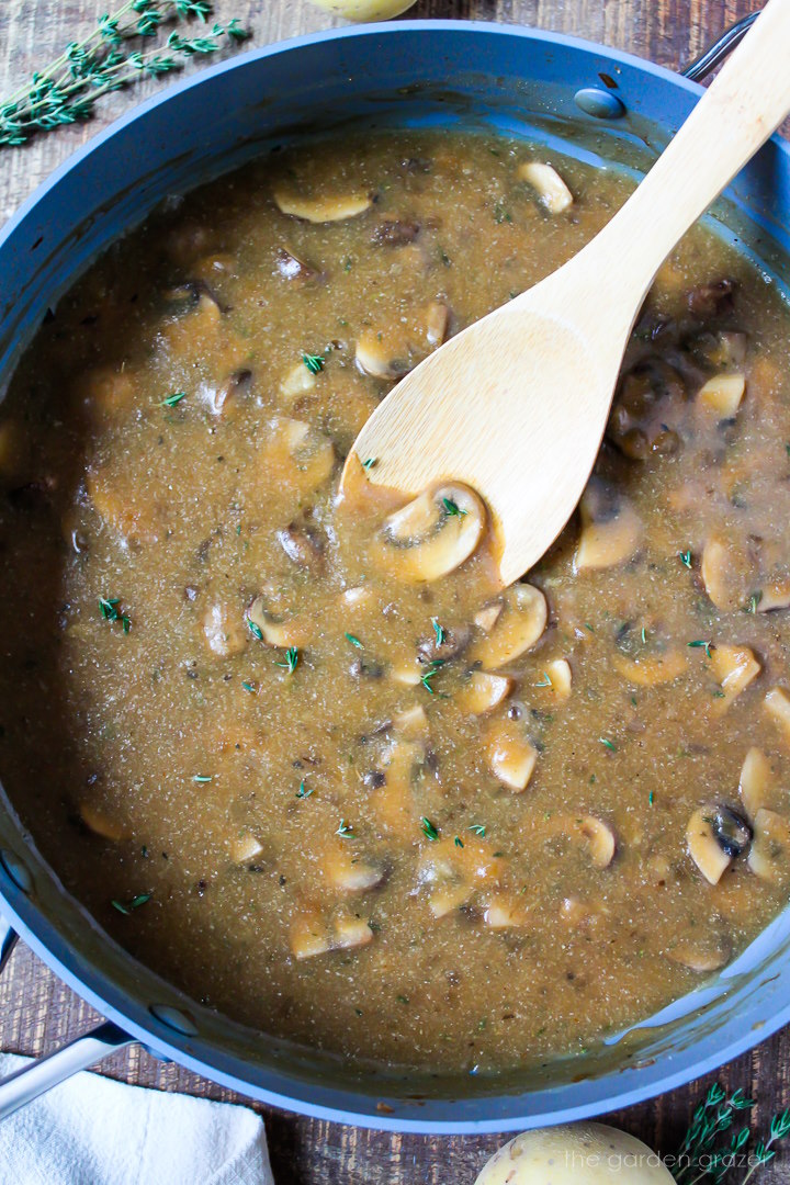 Overhead view of vegan mushroom gravy cooking in a large skillet with wooden stirring spoon