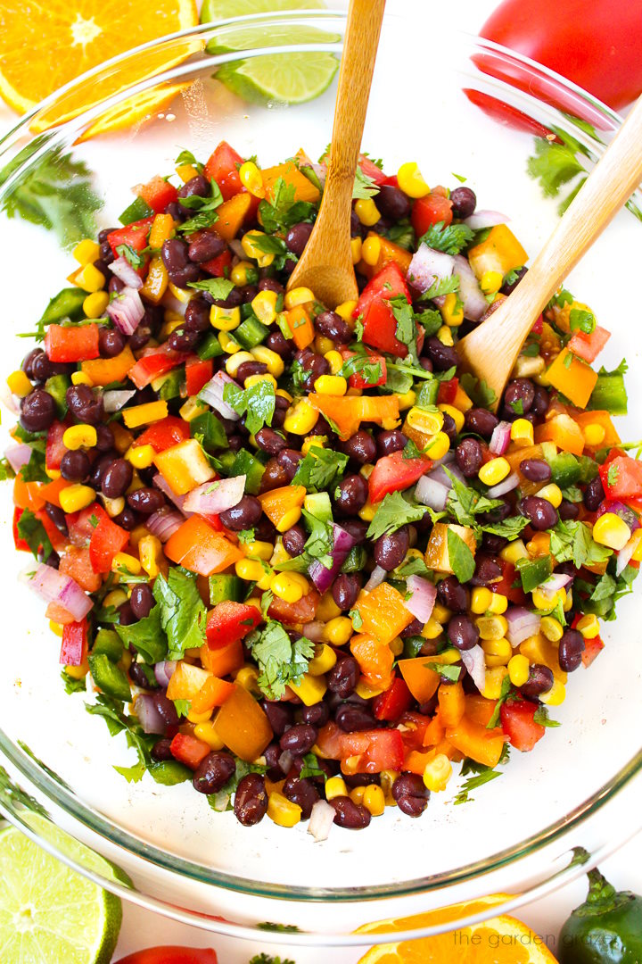 Overhead view of southwest bean salad mixed together in a glass bowl with wooden serving spoons
