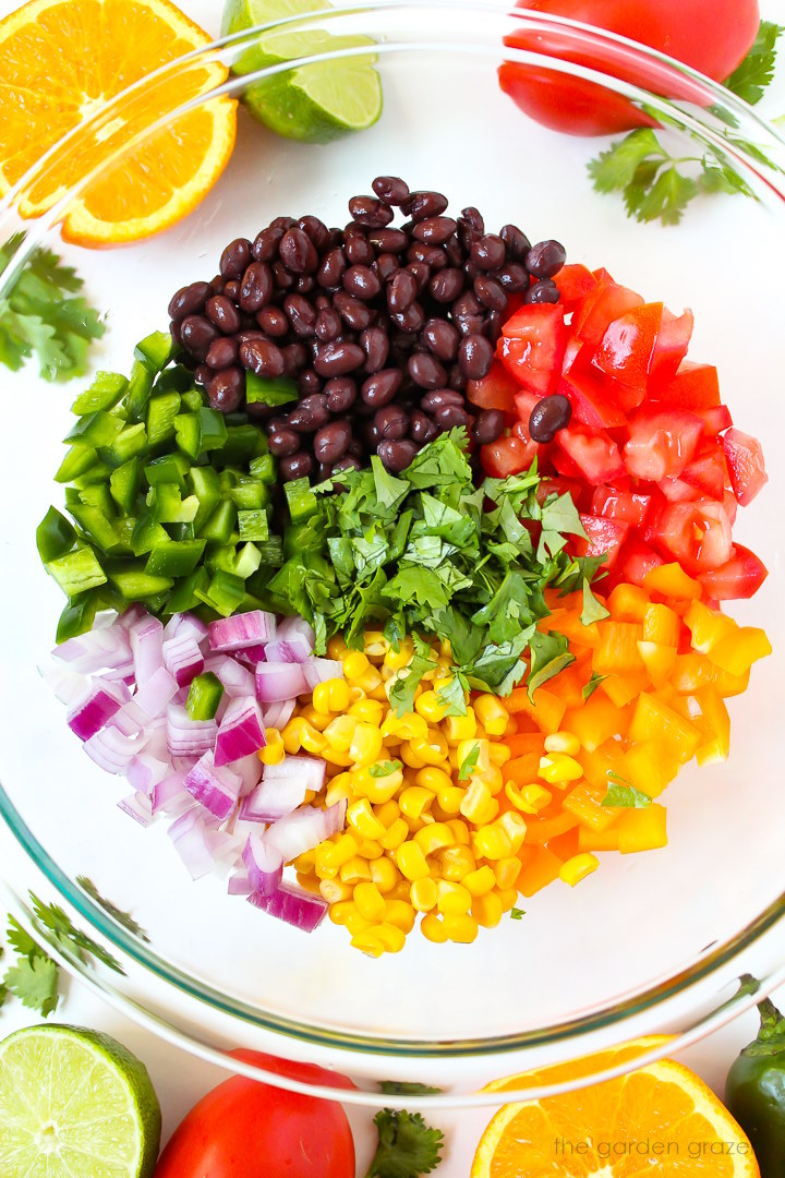 Overhead view of preparing southwest black bean salad in a glass bowl before mixing together