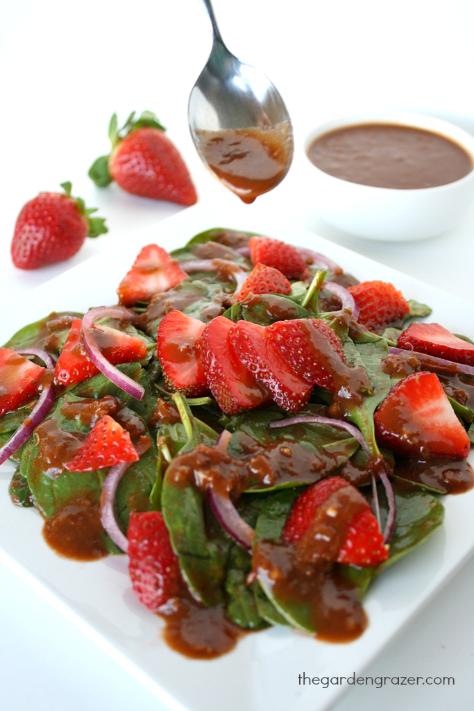Plate of strawberry spinach salad being dressing with balsamic vinaigrette