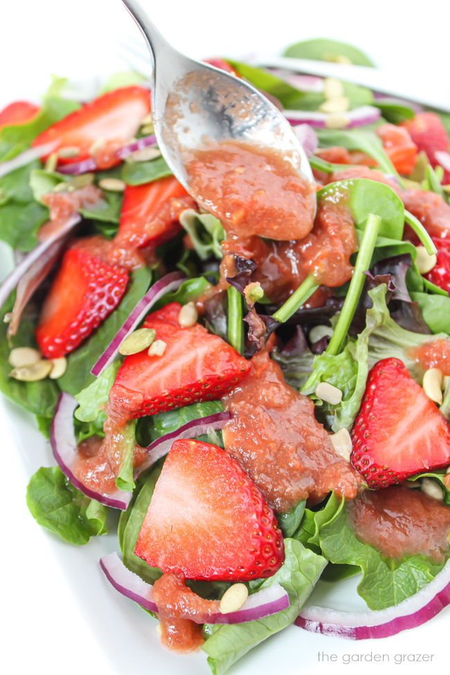 Tomato balsamic dressing being spooned over a spinach salad