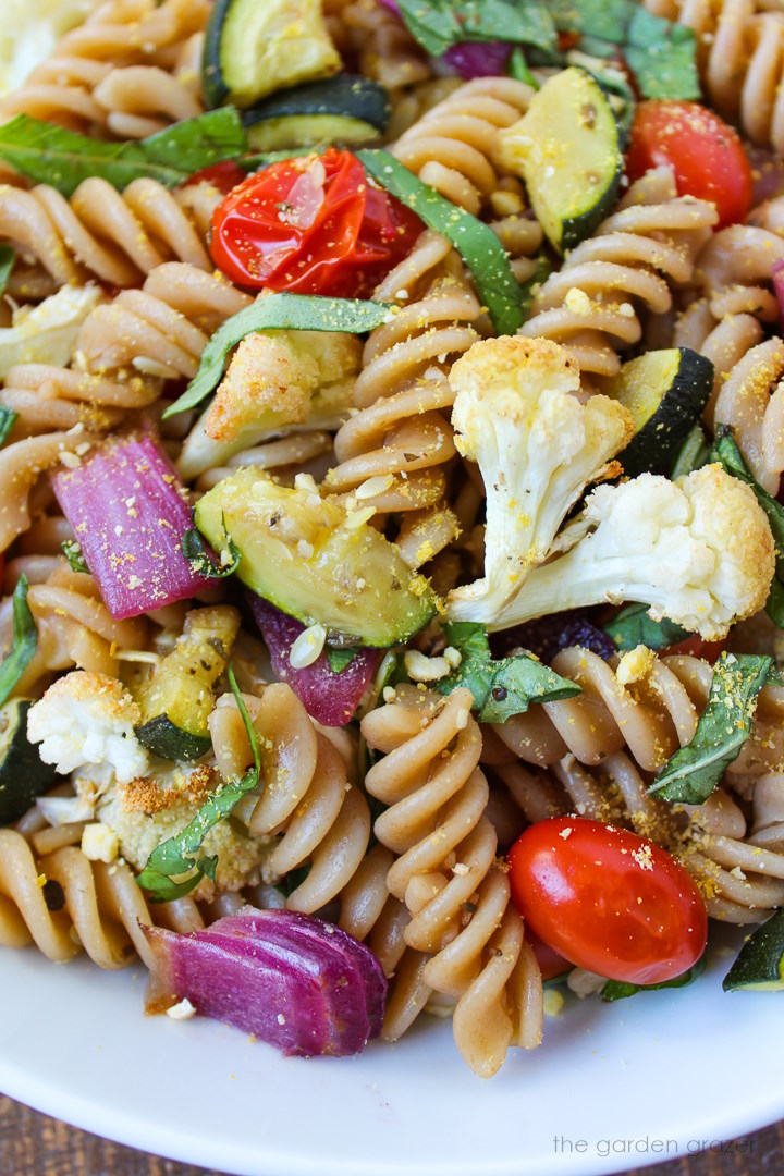 Close up view of roasted vegetable pasta on a white plate with fresh basil and balsamic