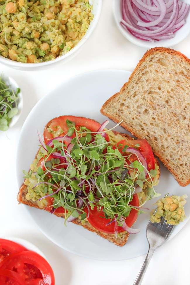 Open-faced sandwich with bread, mashed chickpeas, tomato, and sprouts