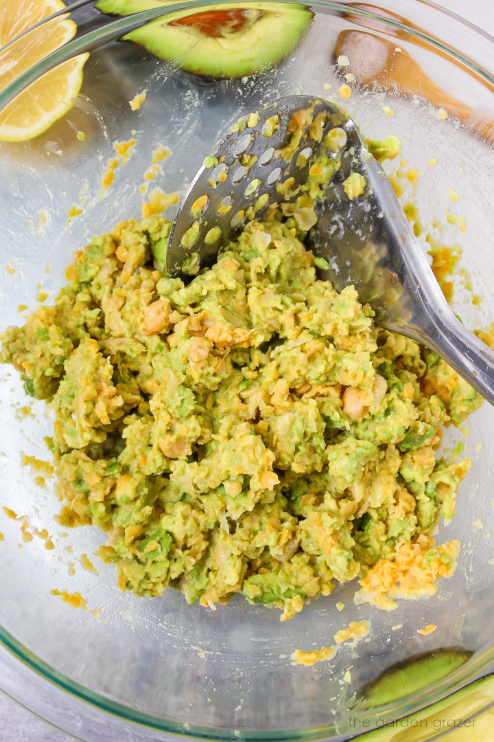 Overhead view of a masher mixing together chickpeas and avocado