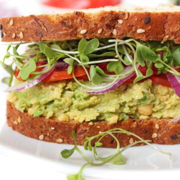 Vegan chickpea avocado mash sandwich with sprouts and tomato on a white plate