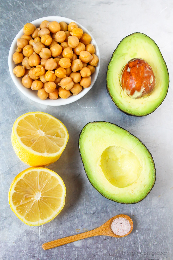 Cooked chickpeas, fresh avocado, lemon, and salt ingredients laid out on a metal tray