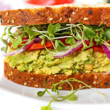 Vegan chickpea avocado mash sandwich with sprouts and tomato on a white plate