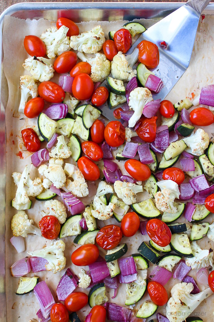 Overhead view of vegetables roasting on a sheet pan with metal spatula