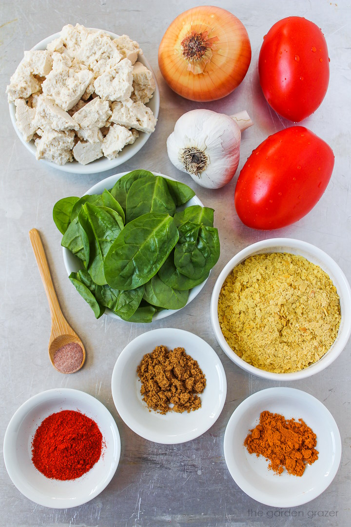 Roma tomatoes, onion, garlic, fresh spinach, nutritional yeast, and spice ingredients laid out on a metal tray