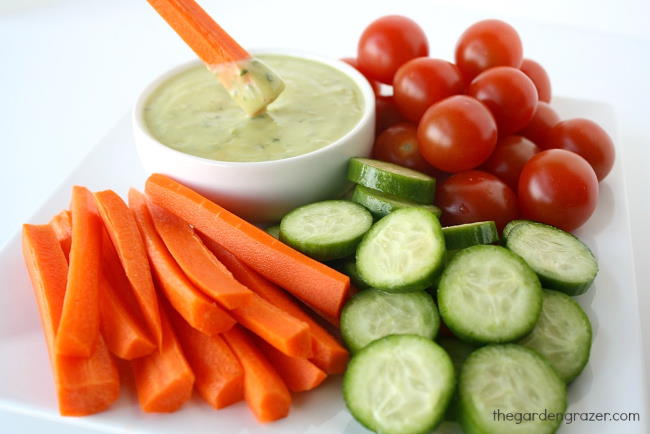 Plate of carrots, cucumbers, and tomatoes with small bowl of dressing
