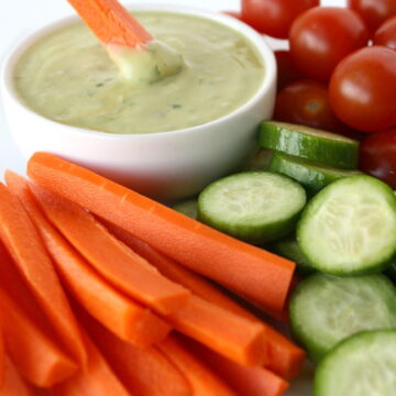 Carrot stick dipping into a bowl of vegan creamy avocado dressing
