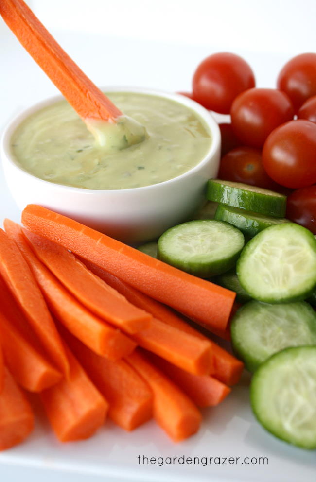 Carrot stick dipping into a bowl of vegan creamy avocado dressing