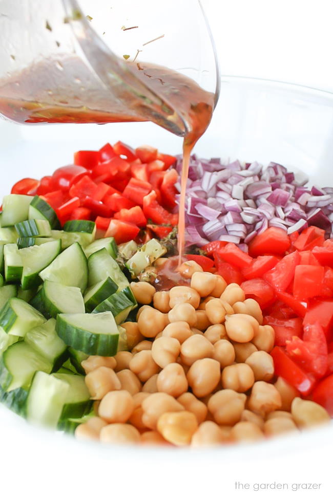 Ingredients for Greek chopped salad in a bowl with dressing being poured on top