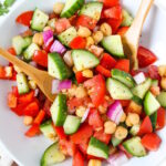Greek Chopped Salad with chickpeas on a white plate with bamboo serving spoons