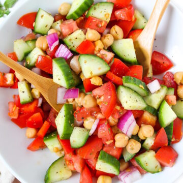 Greek Chopped Salad with chickpeas on a white plate with bamboo serving spoons