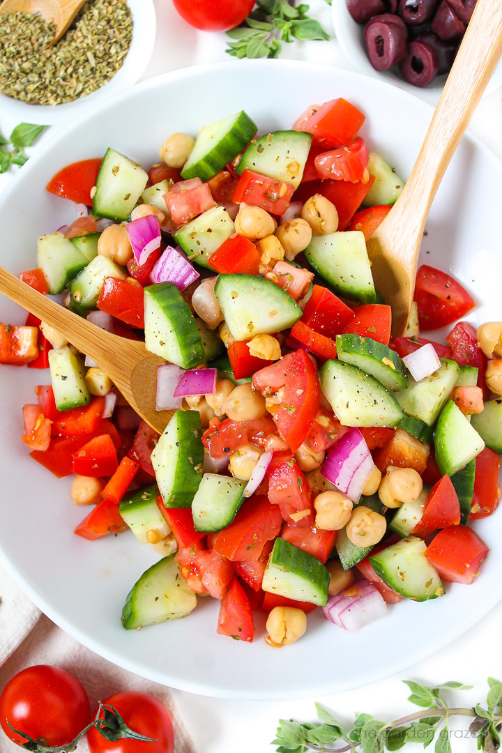 Greek Chopped Salad with chickpeas on a white plate with bamboo serving spoons