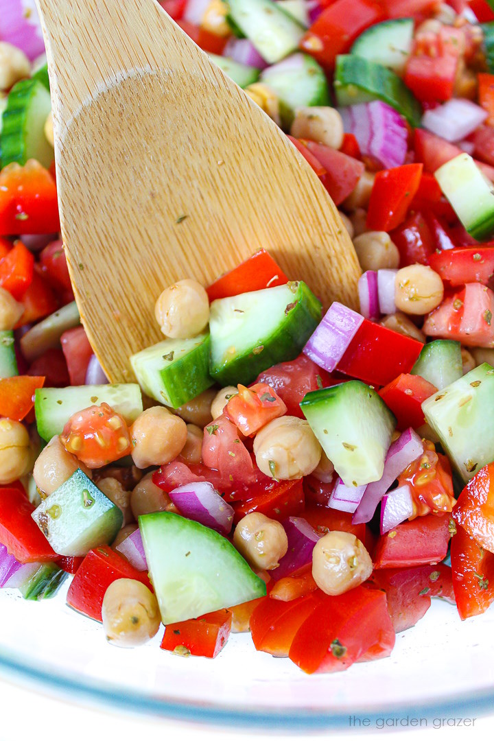 Close up view of a wooden spoon lifting up Greek Chopped Salad from a bowl