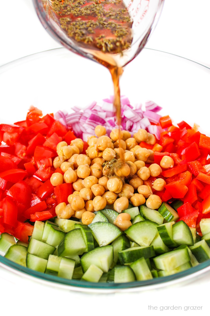 Red wine vinegar dressing being poured over chopped salad ingredients in a large glass bowl