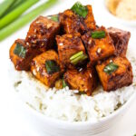 Asian Garlic Tofu with green onions served on a bed of rice in a white bowl