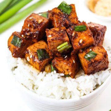 Asian Garlic Tofu with green onions served on a bed of rice in a white bowl