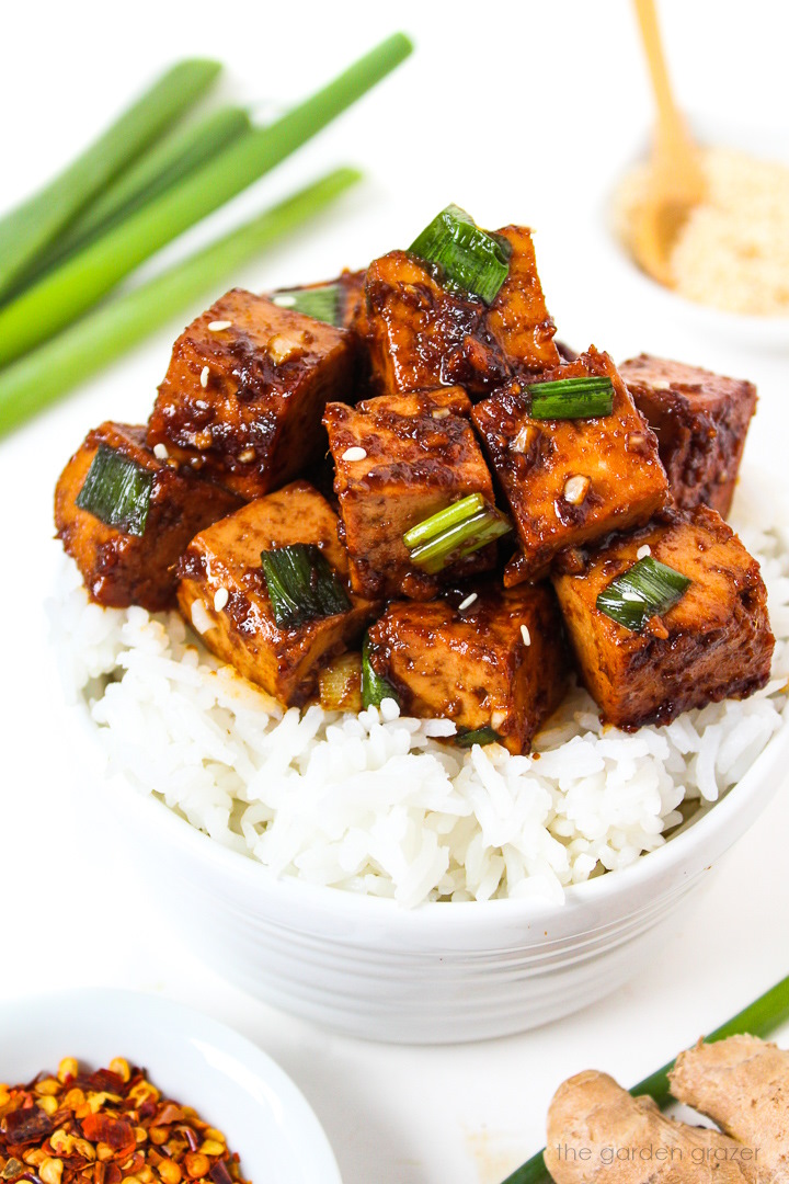 Asian Garlic Tofu with green onions served on a bed of rice in a white bowl