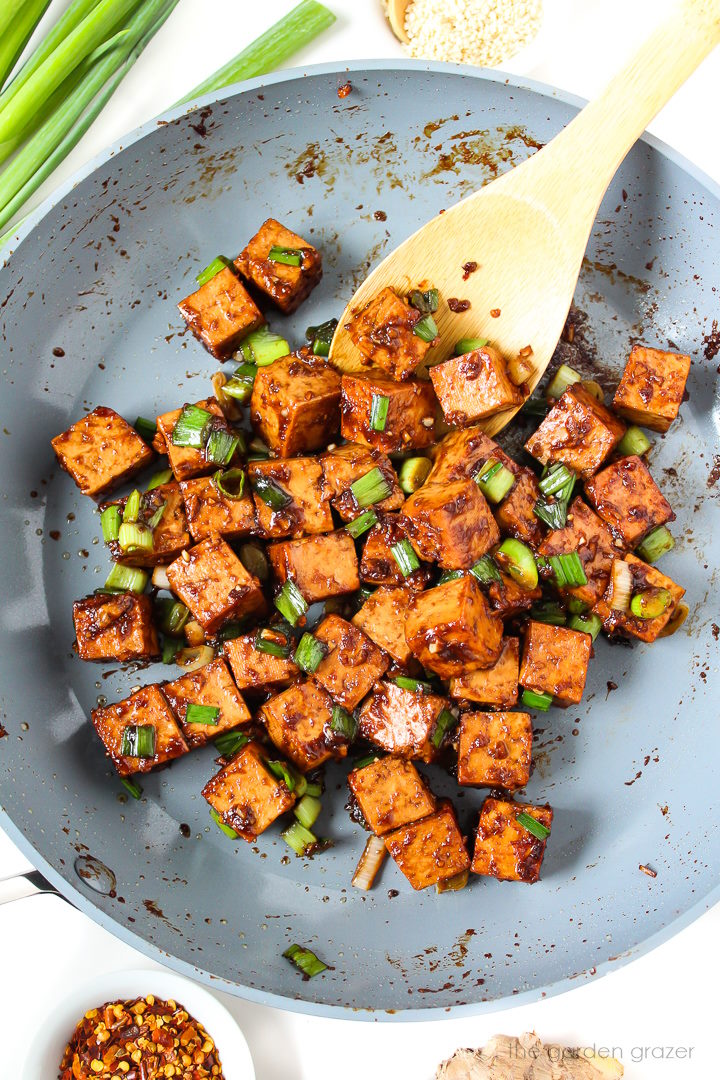 Overhead view of Asian Garlic Tofu cooking in a skillet with wooden stirring spoon