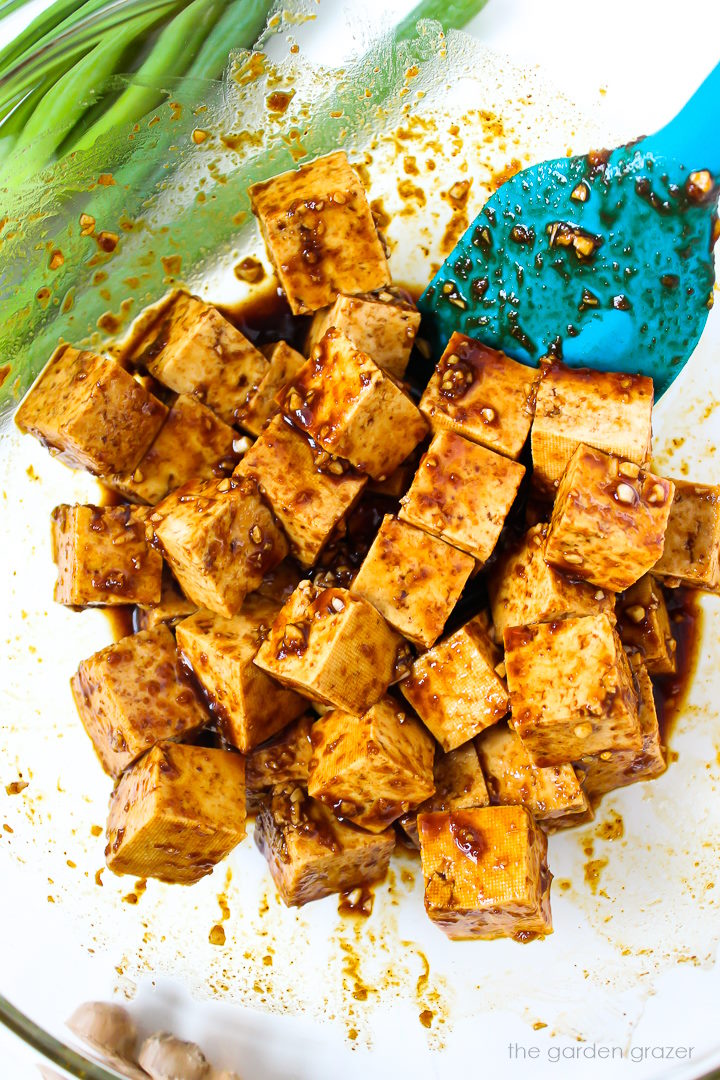 Overhead view of tofu cubes marinating in a glass bowl