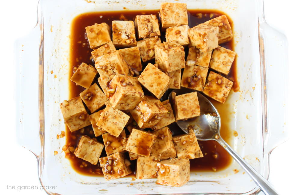 Tofu cubes tossed in a garlic sauce in a shallow glass pan