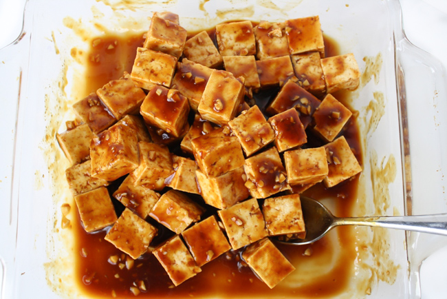 Tofu cubes tossed in an Asian garlic sauce in a shallow glass pan