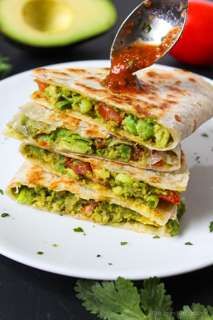 Spooning salsa over a stack of avocado quesadillas on a white plate