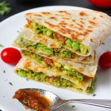 A stack of avocado quesadillas on a white plate with a salsa spoon for serving