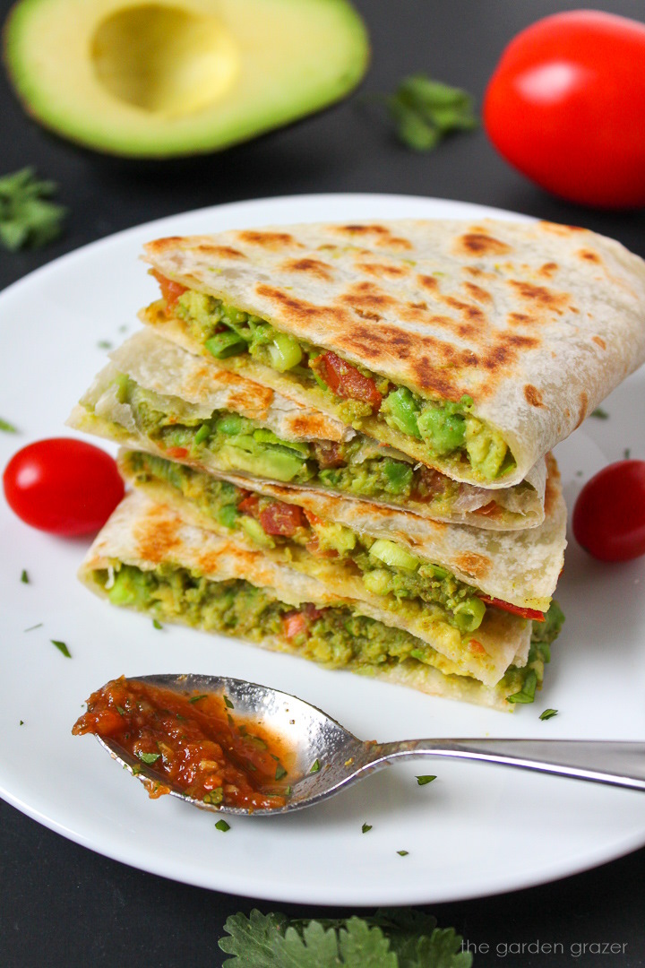 A stack of avocado quesadillas on a white plate with a salsa spoon for serving